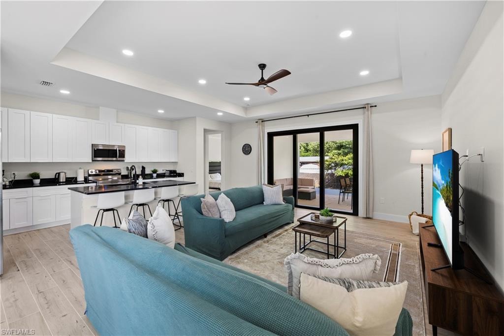 Open-concept living area featuring light wood-finish flooring, recessed lighting, and a tray ceiling