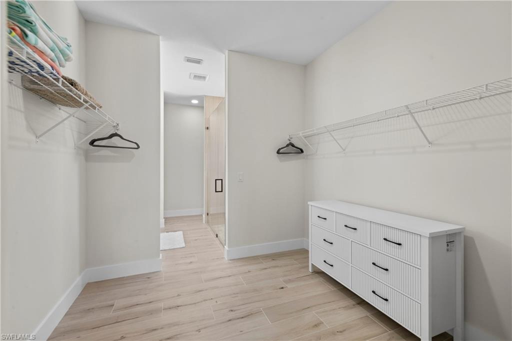Spacious walk-in closet featuring light wood-finish flooring, white wire shelving, and a built-in dresser with black hardware