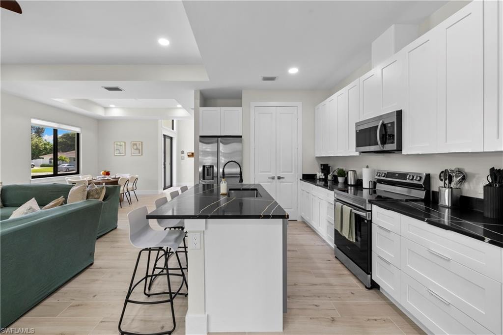 Modern kitchen featuring white shaker cabinetry, dark countertops, stainless steel appliances, a center island with bar seating, and wood-finish flooring