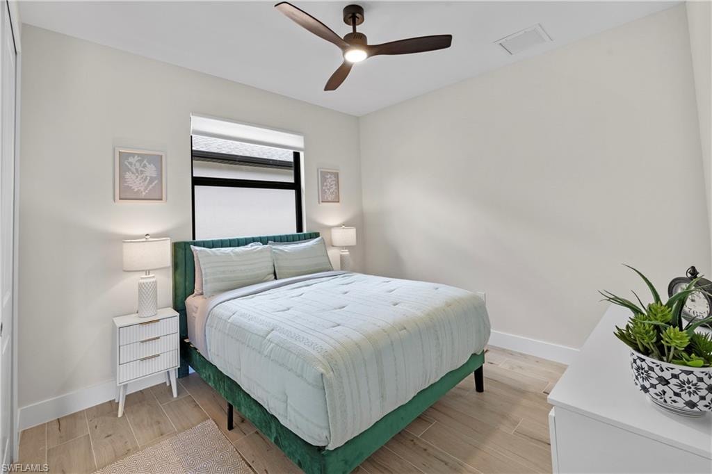Bedroom featuring wood-finish flooring, a window with roller shade, and a ceiling fan with integrated lighting