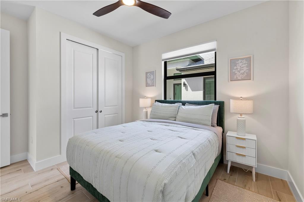 Bedroom featuring light wood-finish flooring, a contemporary ceiling fan, dual sliding closet doors, and a large window with black framing