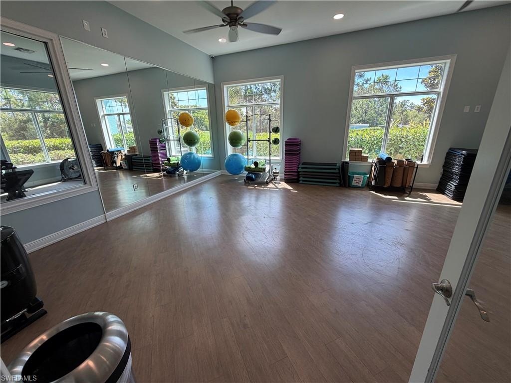 Spacious fitness area featuring wood-finish flooring, ample natural light from multiple large windows, full-wall mirrors, recessed lighting, and a ceiling fan