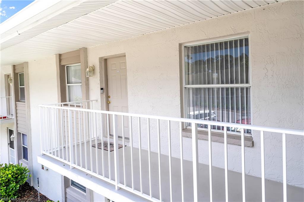 Exterior balcony featuring white metal railings, a textured stucco finish, and a solid entry door with brass-toned hardware