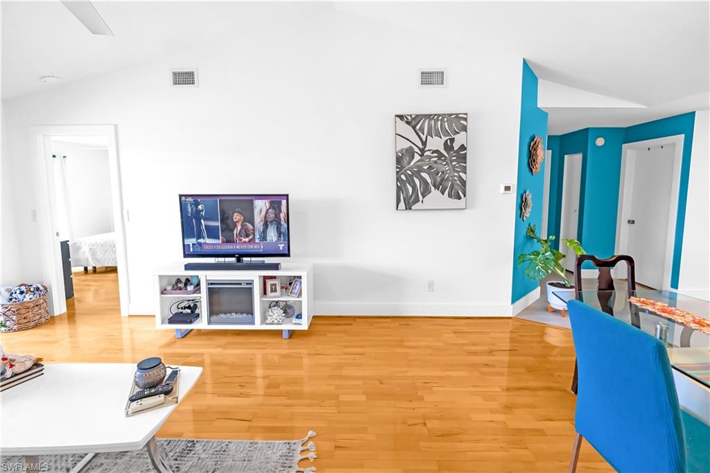 Open-concept living space with vaulted ceilings, wood-finish flooring, and bright white walls