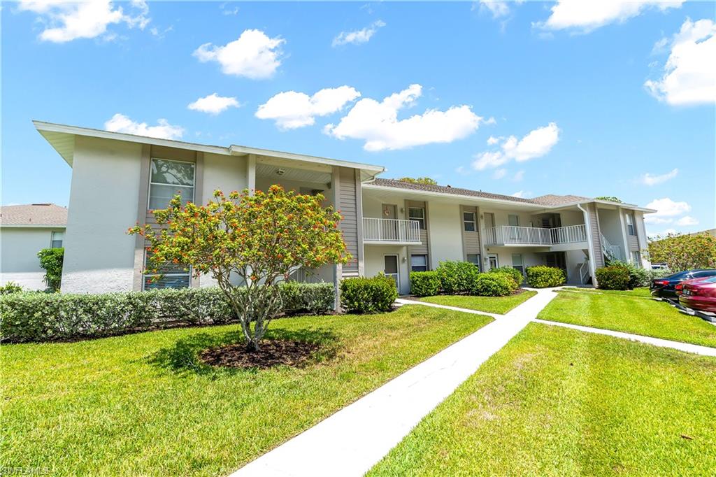 Multi-story building featuring stucco siding, multiple private balconies with white railings, and lush green landscaping