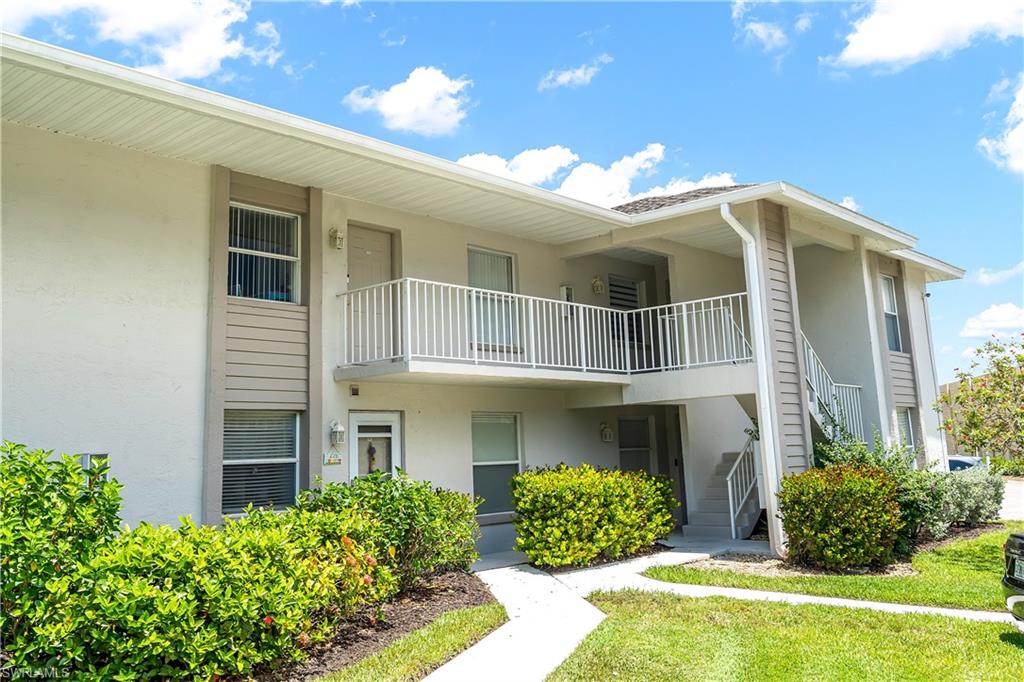 Two-story condominium building featuring a neutral-toned exterior, white railings, and a prominent exterior staircase