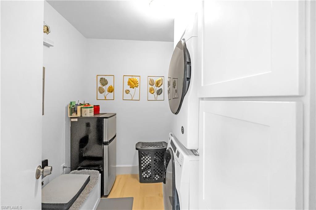 Dedicated laundry area featuring a stacked washer and dryer, light wood-finish flooring, and white baseboards