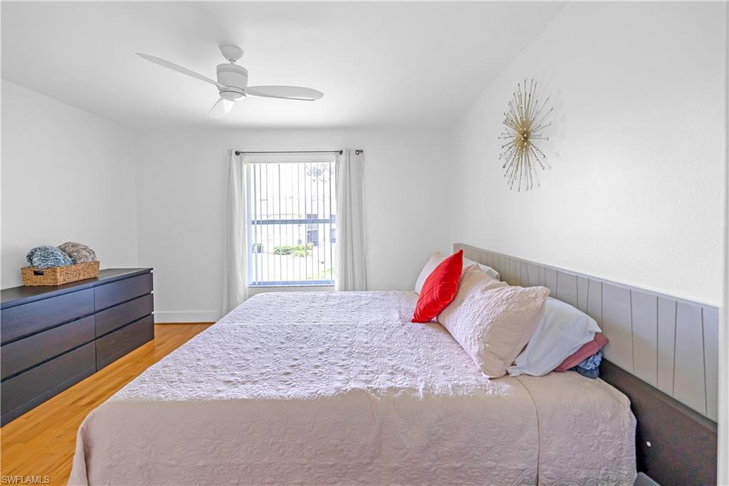 Light-filled room featuring wood-finish flooring, a window with vertical blinds and curtains, a ceiling fan, and a paneled accent wall
