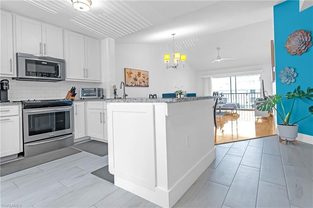 Open-concept kitchen featuring white cabinetry, stainless steel appliances, a subway tile backsplash, and a breakfast bar with stone-finish countertops