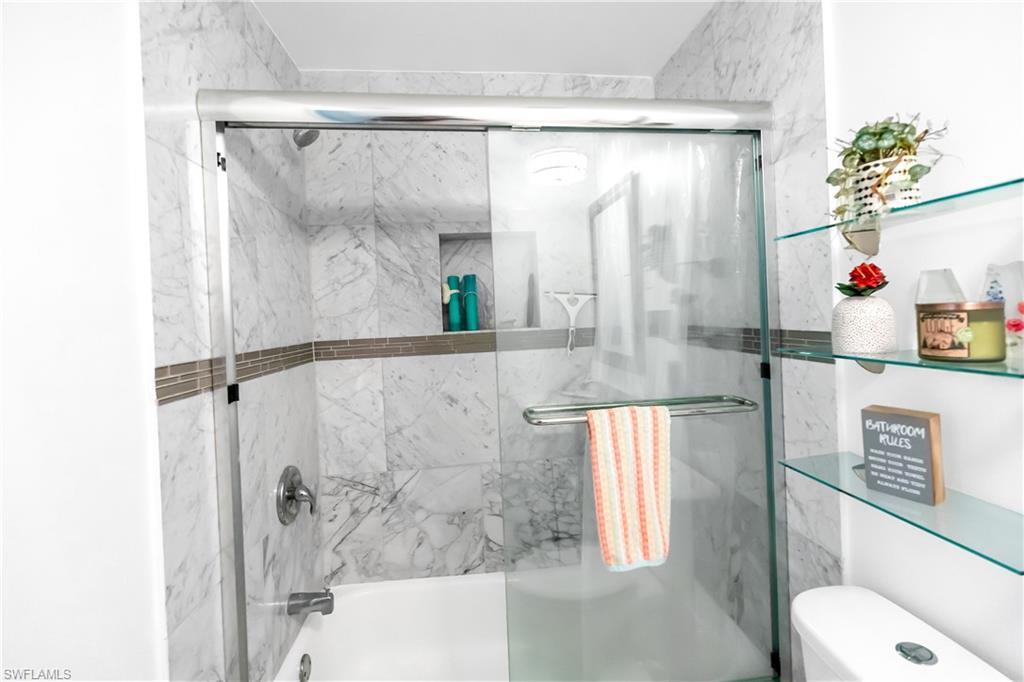 Bathtub and shower combination featuring marble-look wall tiles, a mosaic accent band, and a built-in shower niche