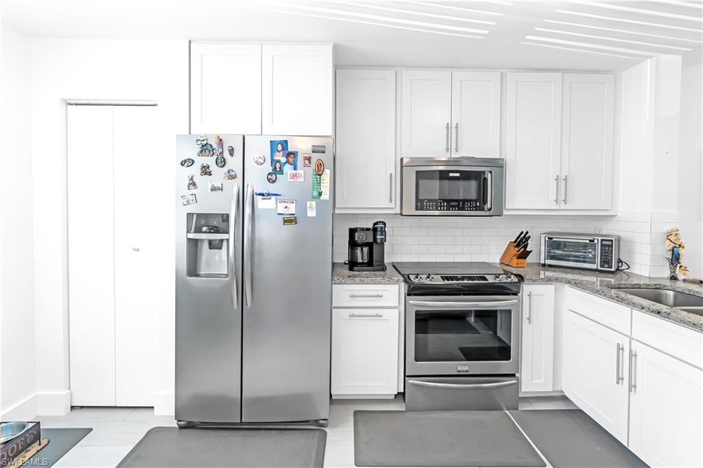 Modern kitchen featuring white shaker cabinetry, stainless steel appliances, speckled countertops, a subway tile backsplash, and light-toned flooring