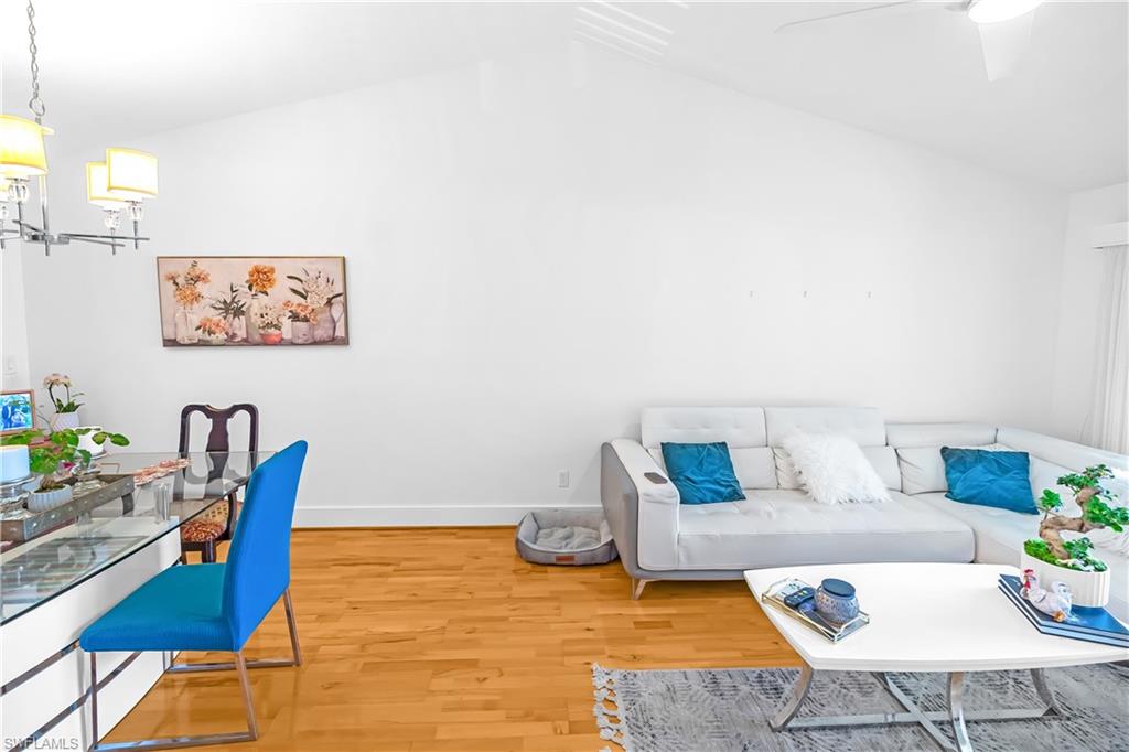 Vaulted ceilings complement wood-finish flooring in this versatile living area, featuring a modern chandelier, ceiling fan, and white walls