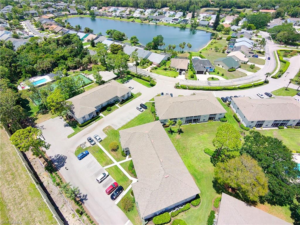 Aerial view of a residential community featuring multiple buildings with shingle roofs, paved parking areas, green lawns, and mature trees