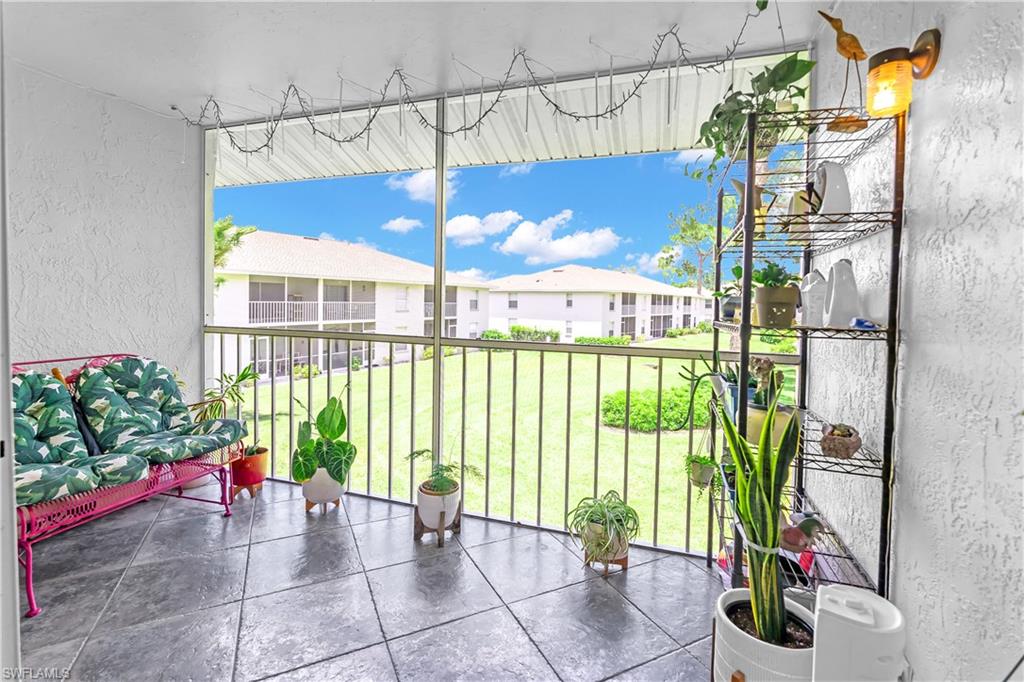 Screened patio featuring dark square tile flooring, white textured walls, and black metal railings overlooking a green lawn