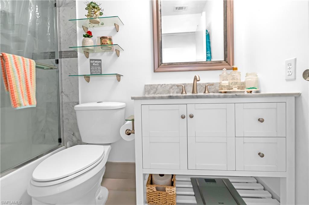 Bathroom featuring a white vanity with a stone countertop, framed mirror, wall-mounted shelving, and a glass-enclosed shower