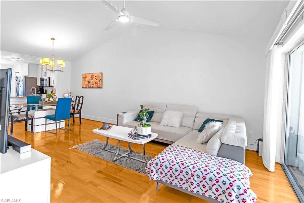 Open-concept living space with vaulted ceilings, wood-finish flooring, a contemporary ceiling fan, and a sliding glass door
