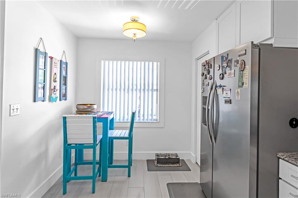 White kitchen featuring wood-finish flooring, a stainless steel refrigerator, white cabinetry, and a window with vertical blinds