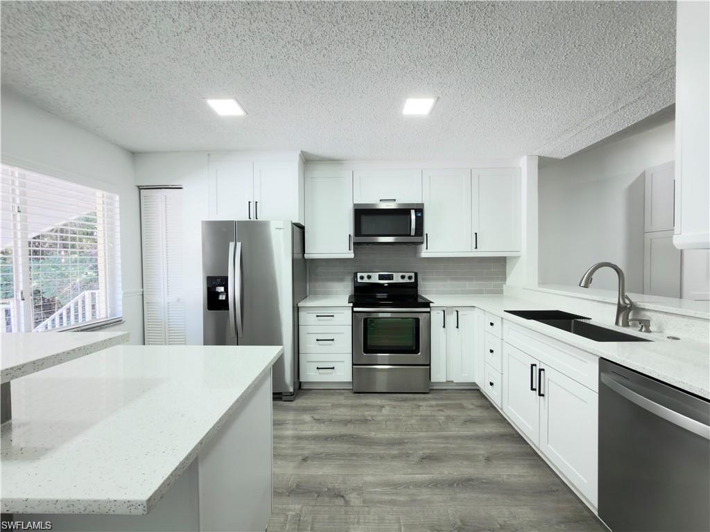 Modern kitchen featuring white shaker cabinetry, light-toned countertops, and wood-finish flooring