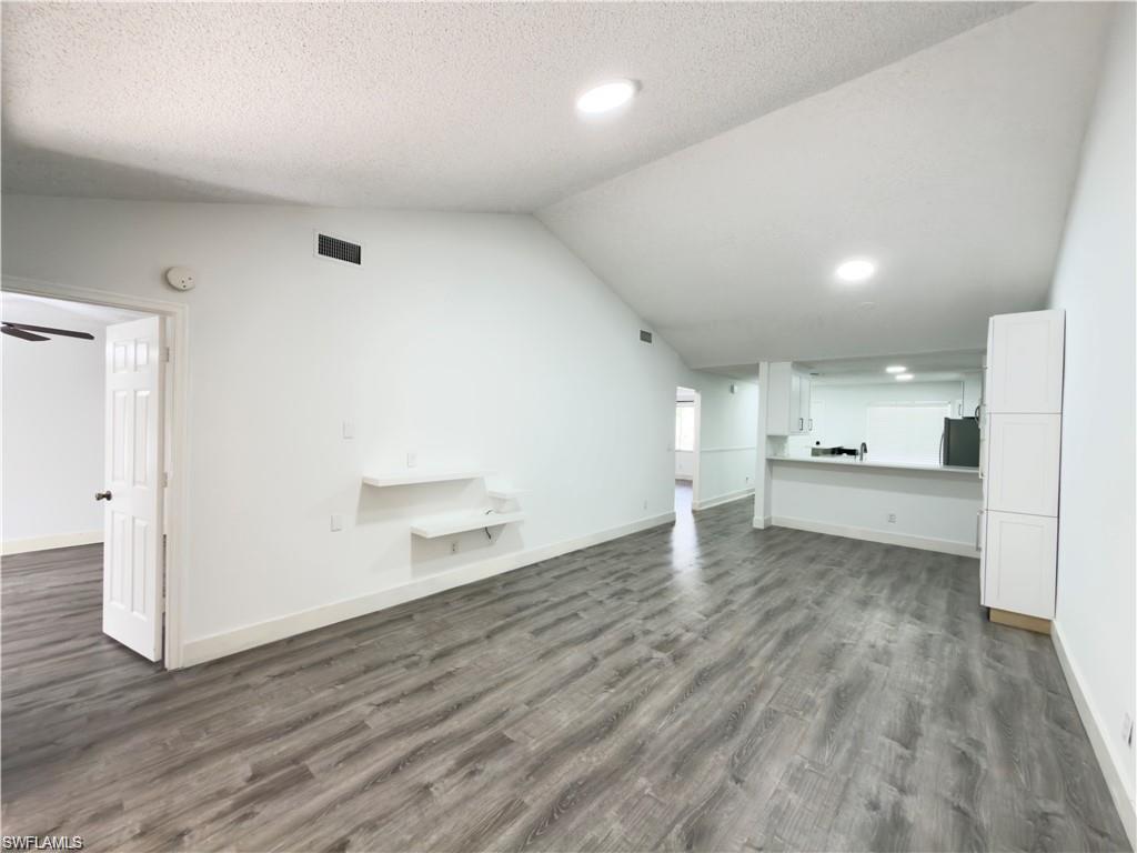 Spacious interior featuring wood-finish flooring, vaulted ceilings, recessed lighting, and a kitchen pass-through with white cabinetry