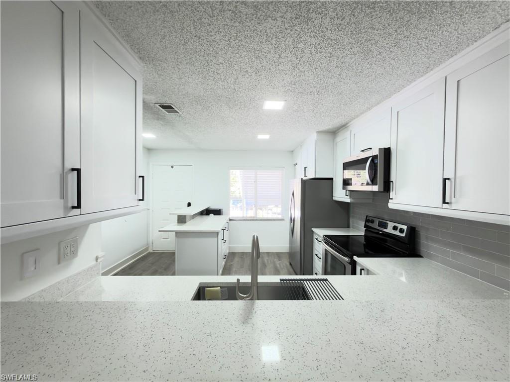 Modern kitchen featuring white shaker cabinetry, stainless steel appliances, speckled white countertops, a sleek subway tile backsplash, and a large undermount sink with a gooseneck faucet