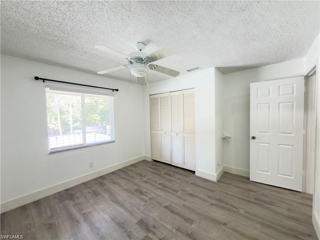 Room featuring wood-finish flooring, a ceiling fan, a window with blinds, and white bi-fold closet doors