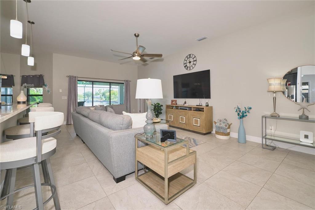 Spacious living area neutral tile flooring, a vaulted ceiling, a ceiling fan, and large sliding glass doors natural light