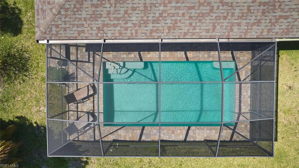 Screened-in swimming pool featuring a rectangular shape, paver decking, and integrated entry steps