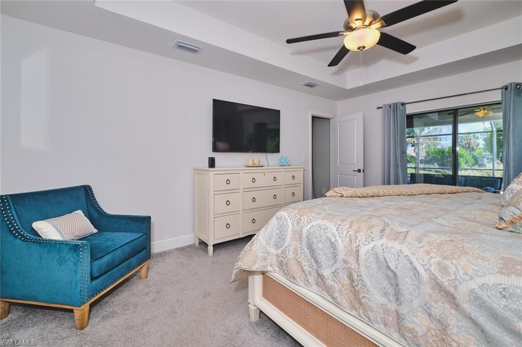 Spacious room featuring tray ceilings with a ceiling fan, plush carpet flooring, and a large sliding glass door with exterior screening