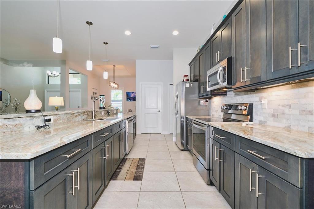 Spacious kitchen featuring extensive counter space with light-toned stone surfaces, dark wood-finish cabinetry, and stainless steel appliances