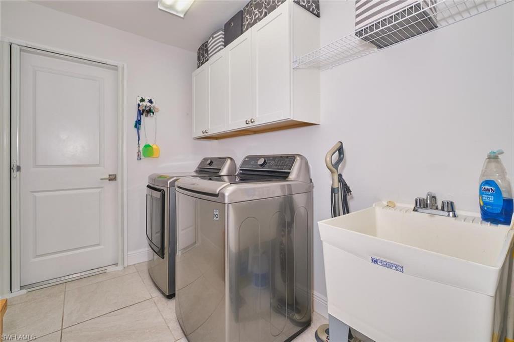 Dedicated laundry space featuring a utility sink, white upper cabinetry, and tile flooring