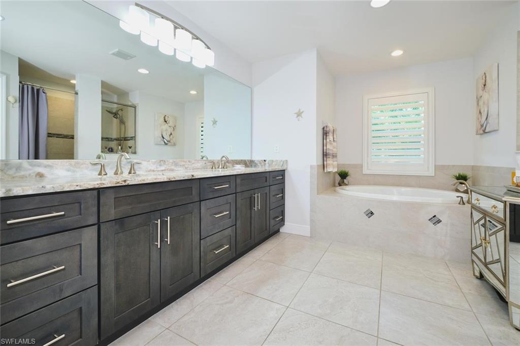 DUAL SINKS vanity with light-toned countertop, a large framed mirror, and a built-in soaking tub with a window above