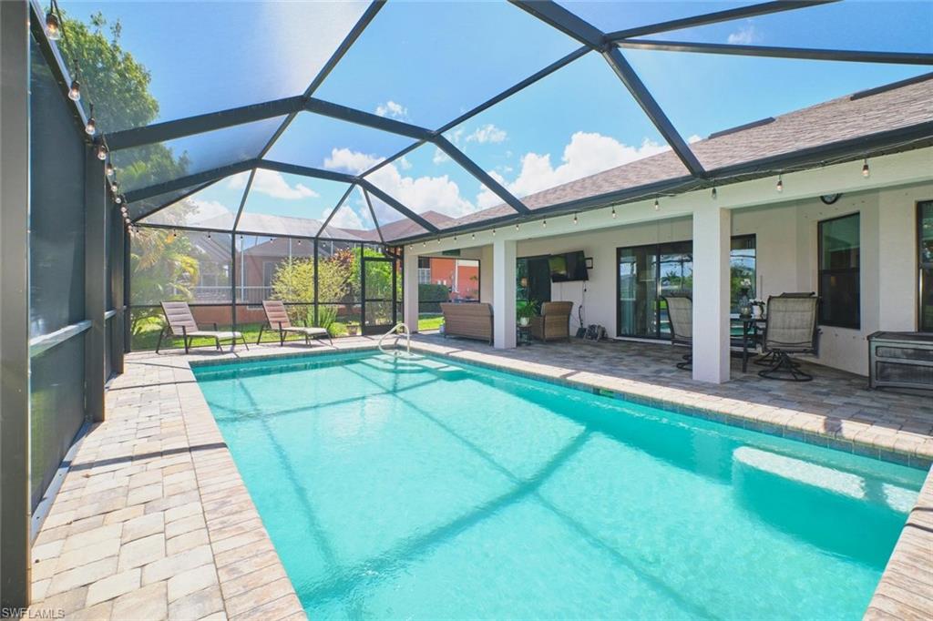 Screened outdoor living area featuring a rectangular pool with integrated steps, a paver patio, an overhead string lighting system, and direct access to the interior via sliding glass doors
