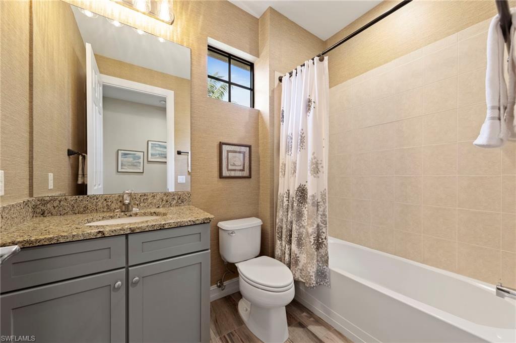 Hall bathroom featuring a granite-topped vanity with undermount sink, gray cabinetry, wood-finish tile flooring, and a window above the toilet. NEW TILE FLOOR (2018), NEW WALLPAPER (2018)