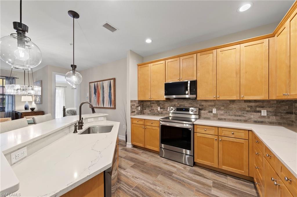 Kitchen featuring light wood cabinetry, stainless steel appliances, stone tile backsplash, and light-toned countertops.NEW KITCHEN LG-IQ APPLIANCES (2024), NEW GARBAGE DISPOSAL (2022), NEW QUARTZ COUNTERS (2018), NEW BACKSPLASH (2018), NEW TILE FLOOR (2018)