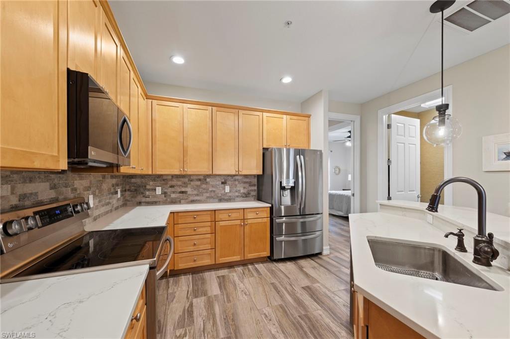 Kitchen featuring wood cabinetry, stainless steel appliances, white countertops, a tiled backsplash, and wood-finish flooring.NEW KITCHEN LG-IQ APPLIANCES (2024), NEW GARBAGE DISPOSAL (2022), NEW QUARTZ COUNTERS (2018), NEW BACKSPLASH (2018), NEW TILE FLOOR (2018)