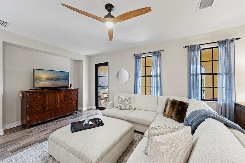 Spacious living area featuring wood-finish flooring, a modern ceiling fan, and multiple windows with dark frames. NEW TILE FLOOR (2018)