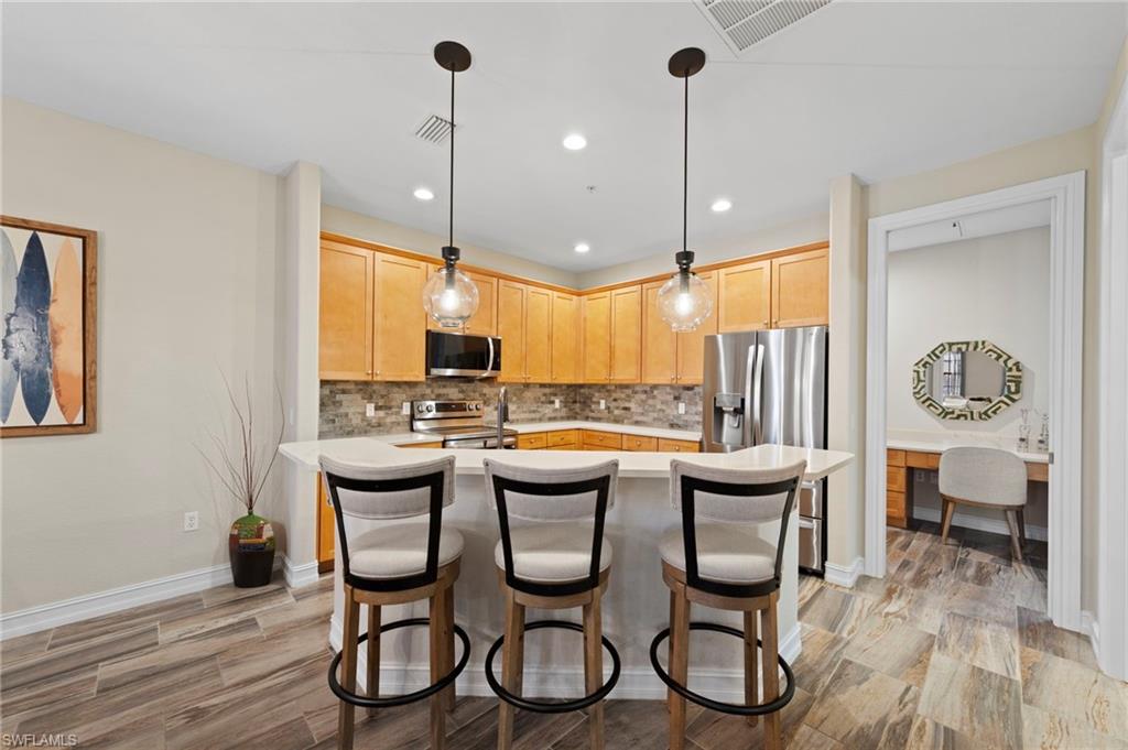 Kitchen featuring wood-finish cabinetry, stainless steel appliances, a tile backsplash, and a breakfast bar with pendant lighting. NEW KITCHEN LG-IQ APPLIANCES (2024), NEW QUARTZ COUNTERS (2018), NEW BACKSPLASH (2018), NEW TILE FLOOR (2018)