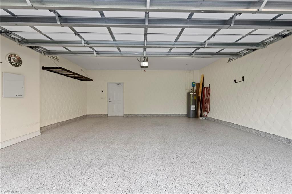 Spacious garage featuring a durable epoxy-finished floor, patterned wall textures, an integrated overhead storage rack, and interior door access. NEW HEAVY DUTY EPOXY FLOOR (2024), NEW HANGING STORAGE SHELVES (2021), NEW WATER HEATER (2016)