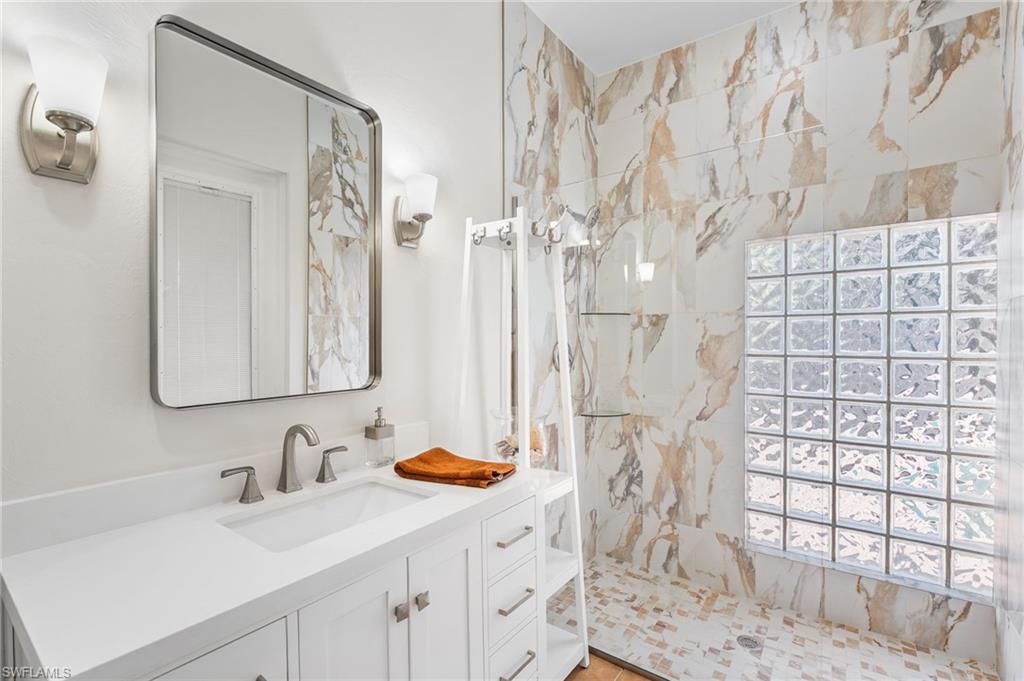 The second full bath is ideally designed as a dedicated pool bath, allowing effortless convenience without ever tracking through the home in wet attire. Just steps from the exterior entry, you are welcomed into a stunning walk-in shower adorned with floor-to-ceiling porcelain tile, paired with a sleek single vanity topped in quartz. An expansive glass block opening floods the space with natural light, enhancing the spa-like ambiance and refined coastal elegance.