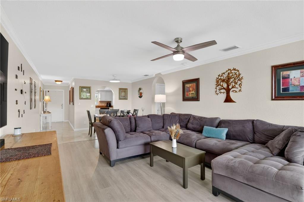 Open-concept living area featuring light wood-finish flooring, a contemporary ceiling fan with integrated lighting, and crown molding