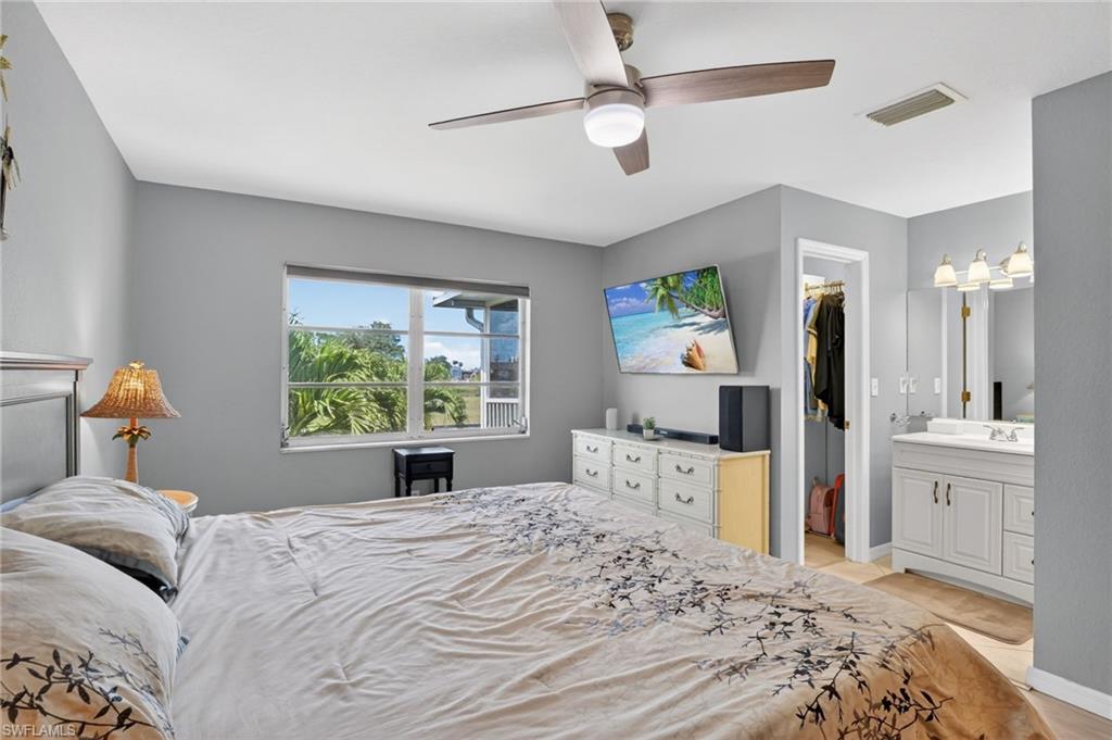 Bedroom featuring a ceiling fan with integrated lighting, a window with exterior landscaping, and direct access to a vanity area