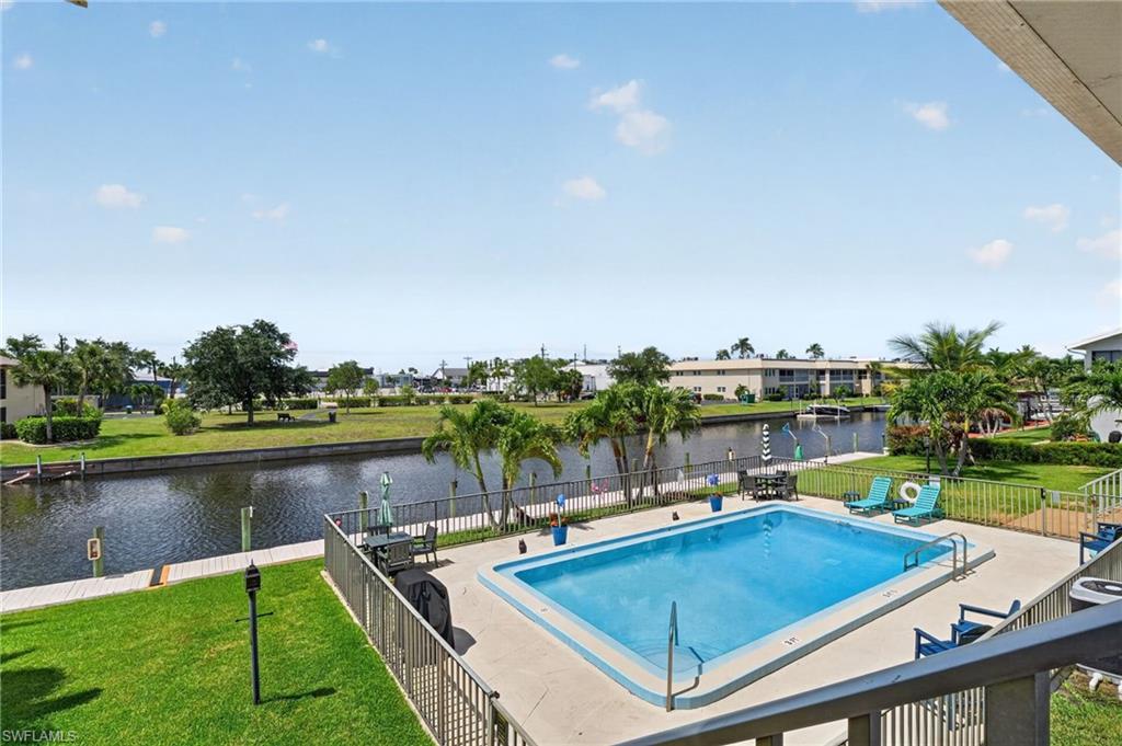 Outdoor swimming pool with concrete decking, surrounded by a metal fence and manicured lawn