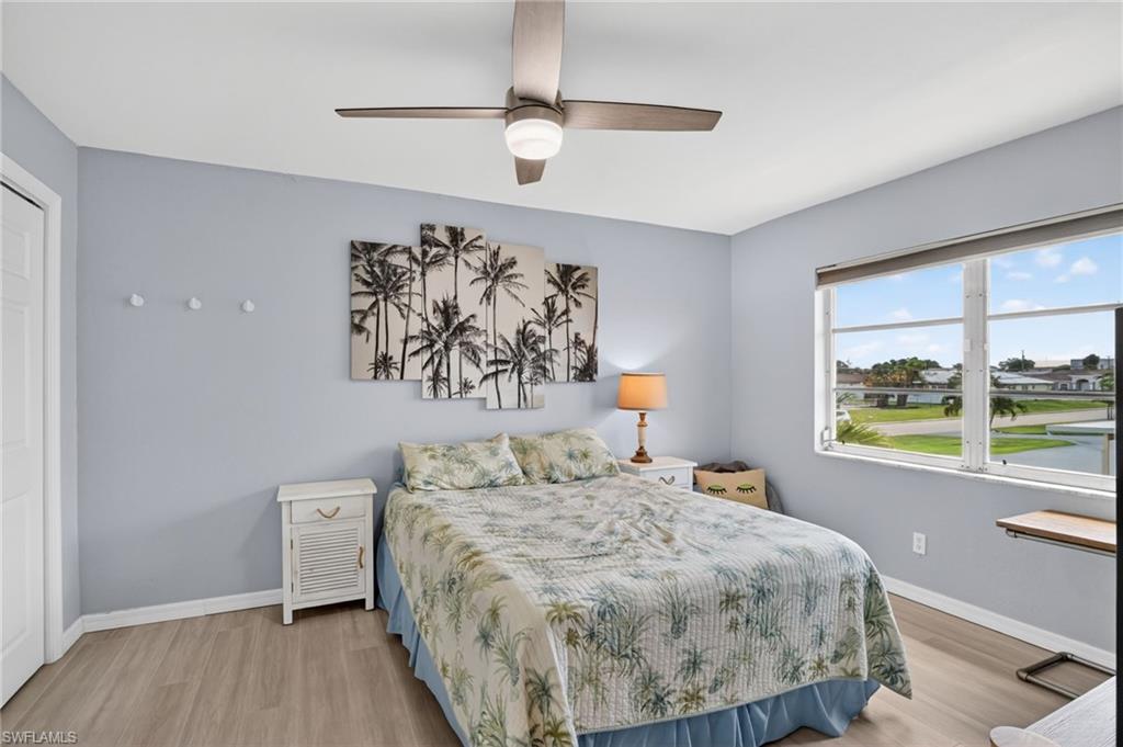 Bedroom featuring wood-finish flooring, a ceiling fan with integrated lighting, and a window offering a waterside perspective