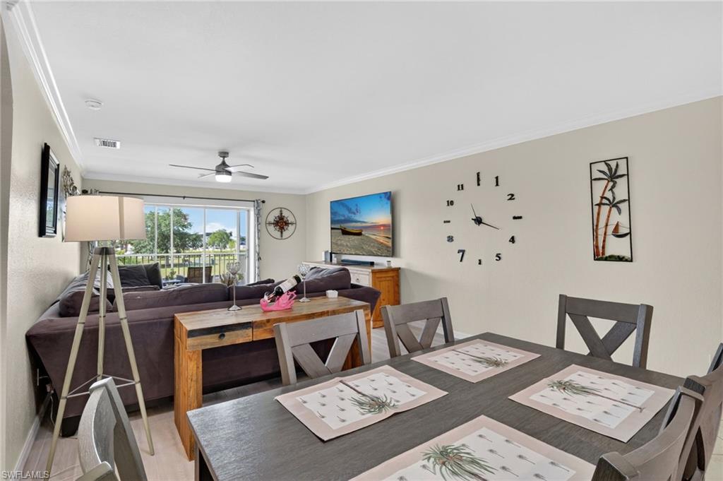 Open-concept living and dining area featuring light-toned walls, crown molding, and wood-finish flooring