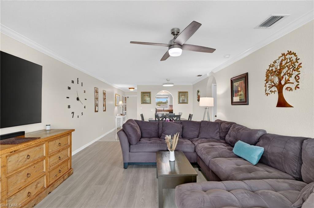 Spacious living area featuring light-toned walls, crown molding, and wood-finish flooring