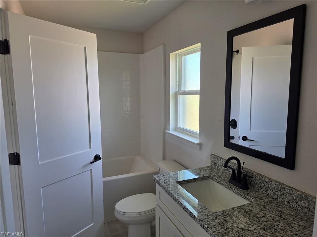 Bathroom featuring a white bathtub with subway tile surround, single-pane window, vanity with granite countertop and undermount sink, and black-framed mirror