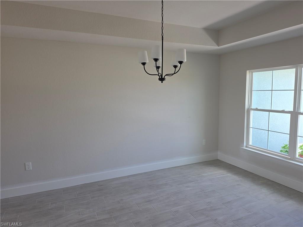 Tray ceiling accentuating the room's height, contemporary chandelier with four lights, large window with privacy film, light-toned wood-finish tile flooring, and clean baseboard trim