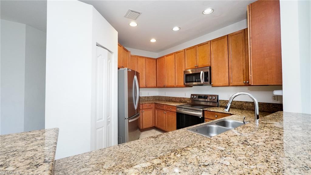Kitchen featuring granite countertops, stainless steel appliances, wood-finish cabinetry, a double basin sink, and recessed lighting