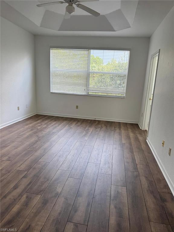 Spacious room featuring wood-finish flooring, a tray ceiling, and a ceiling fan with integrated lighting