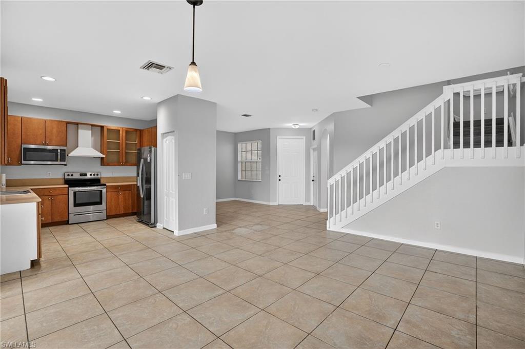 Open-concept living area with large format tile flooring, a kitchen featuring wood cabinetry and stainless steel appliances, a white staircase with balusters, and recessed lighting